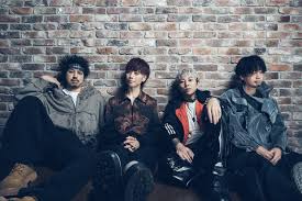 ASH DA HERO | The Outerhaven Four young men sit against a brick wall, posing together like a band photo with casual clothing.