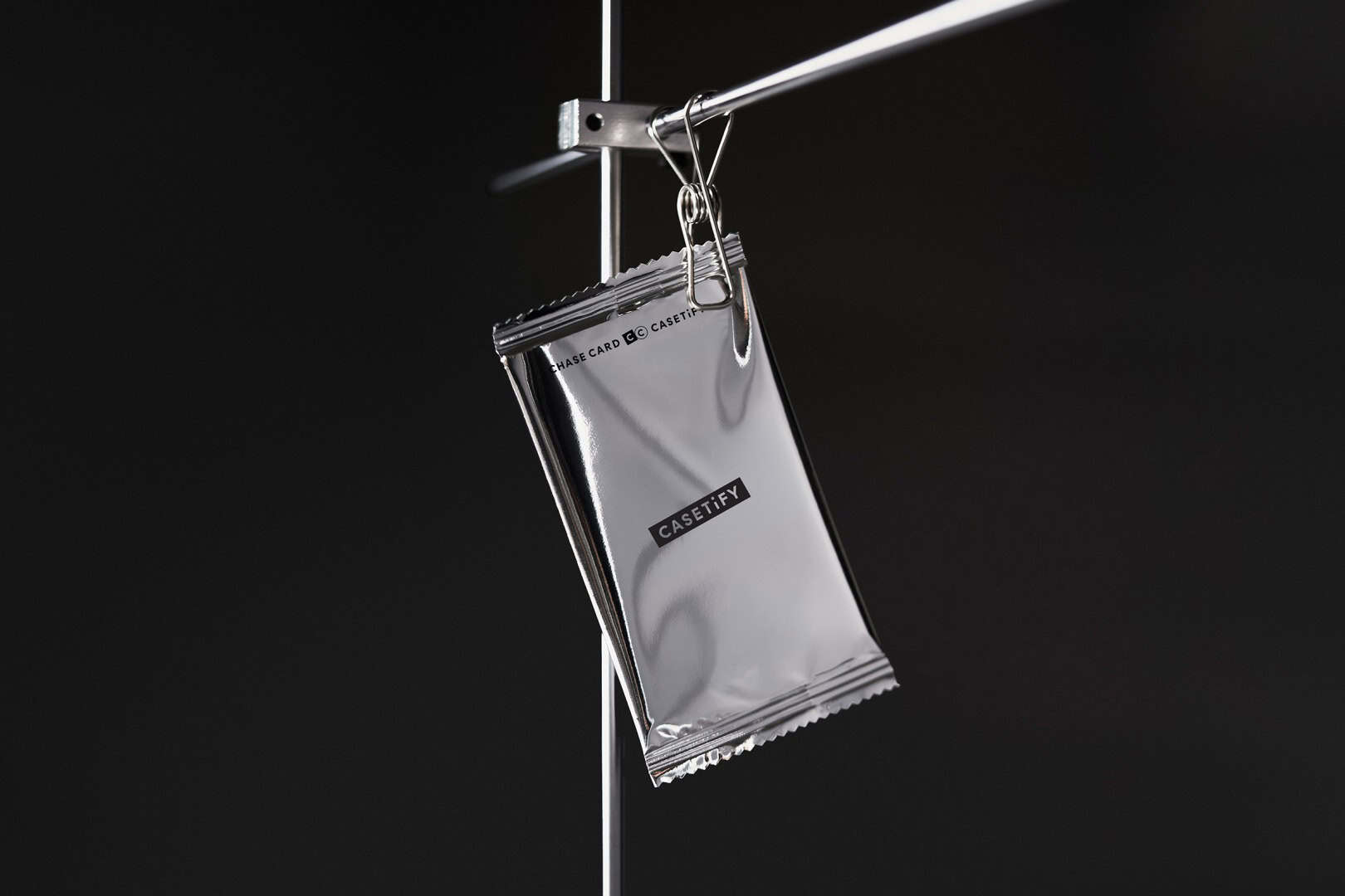 Casetify Cards 4 | The Outerhaven Shiny silver Casetify packaging hanging from a metal rod with a clip against a dark background, showcasing the product packaging integrity and branding.