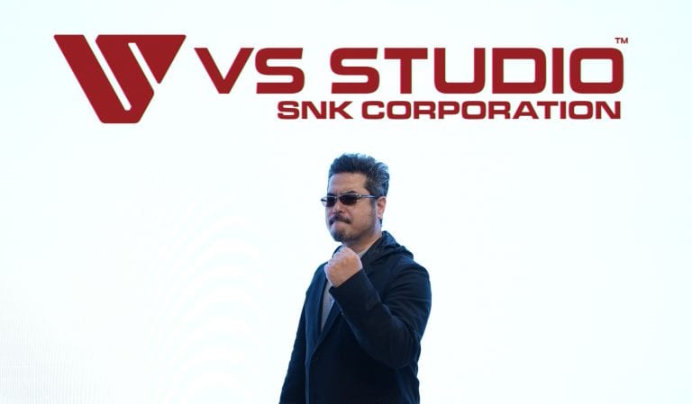 HIGvYUobsAAuY09 | The Outerhaven Man in a dark suit and sunglasses raises a clenched fist beneath a large red VS STUDIO SNK CORPORATION logo.