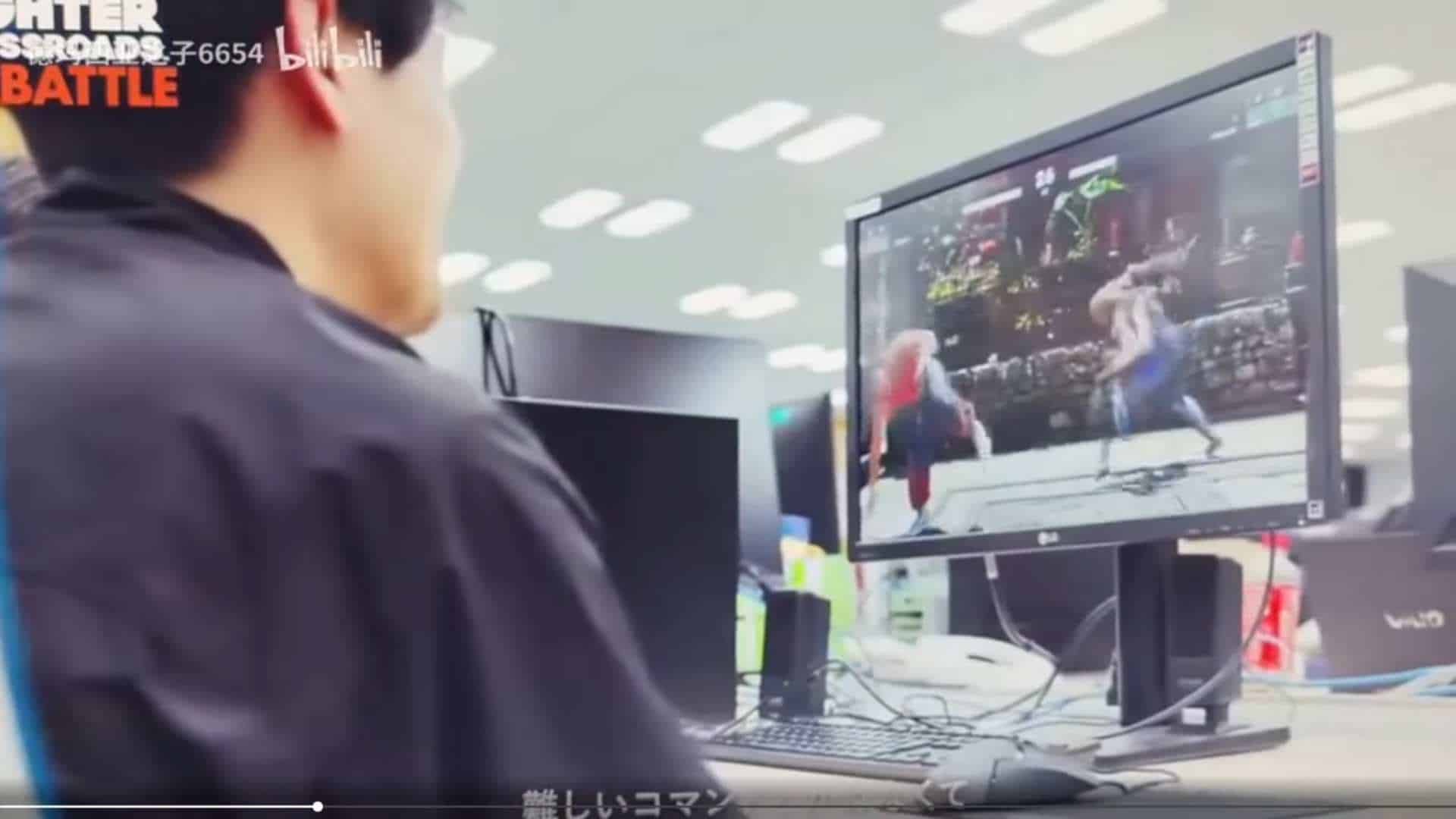 Person sitting at a desk, facing away, watching a video on a large computer monitor in an office setting.