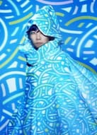 kz | The Outerhaven Person in a blue patterned hooded cloak posing against a blue geometric backdrop.