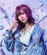 picco | The Outerhaven Portrait of a young woman with purple hair wearing a blue patterned jacket, posing against a crystal-like blue background.