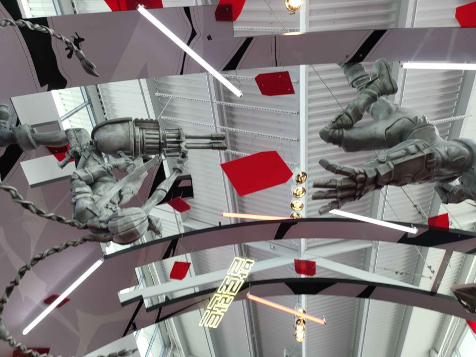 Two large silver armored hands suspended by chains reach toward each other over a glossy curved surface with red geometric panels and bright lights.