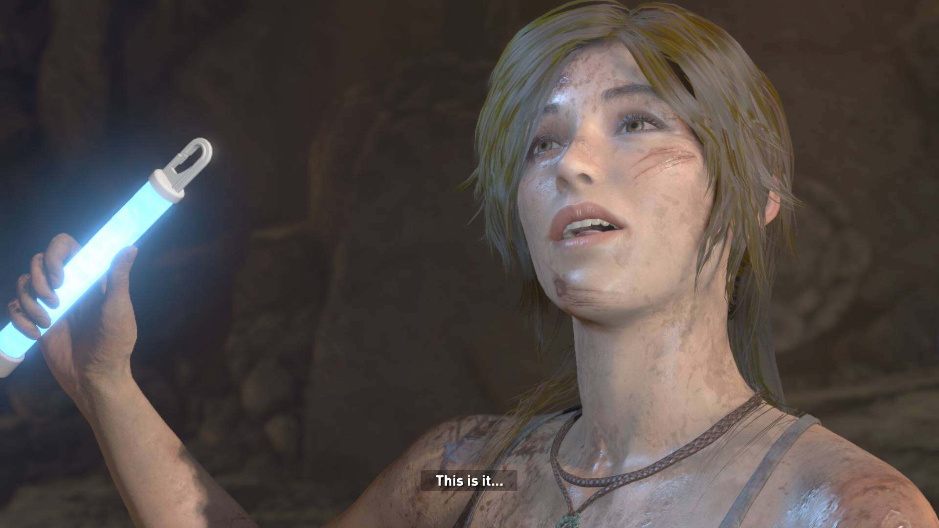 20260628214748-01KVNFMRB7W22P44K5Z87YZ5FN | The Outerhaven Woman with dirt on her face holds a glowing blue light baton, looking upward in a dim cave; caption reads 'This is it...'