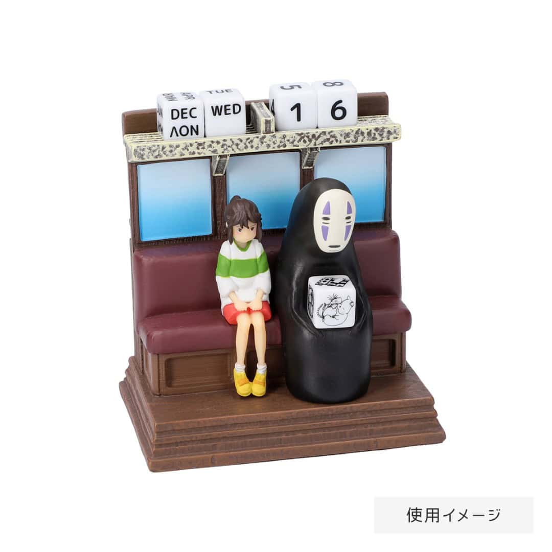 4 Riding the Railway Perpetual Calendar Spirited Away | The Outerhaven Tiny figurine scene: a girl in a green sweater and orange shorts sits on a bench with a black No Face figure, calendar blocks on top.