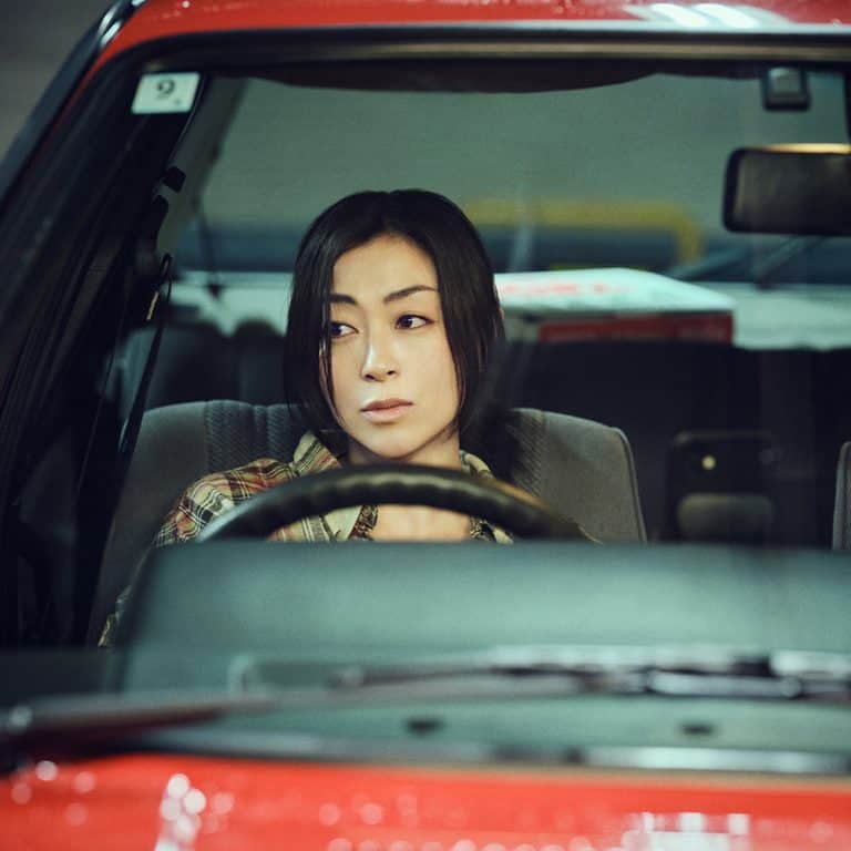 HU_papaparadise | The Outerhaven Woman sitting in the driver's seat of a red car, looking to her left.