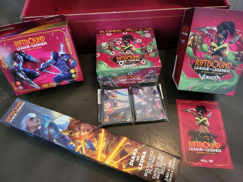 20260717_153154 | The Outerhaven Assorted Riftbound League of Legends trading card game boxes and loose cards on a dark table in a display setup.