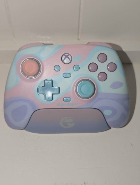 Gamesir FI Front | The Outerhaven Pastel-colored wireless game controller with pink left stick and cyan right stick on a white surface, decorative swirls in pink, blue, and purple.