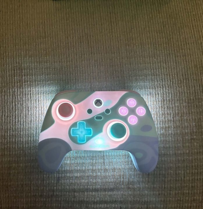 Gamesir RGB Front | The Outerhaven Colorful game controller with pink, teal, and purple patterns on a dark carpet, featuring teal glowing thumbsticks and a bright blue D-pad (informative image).