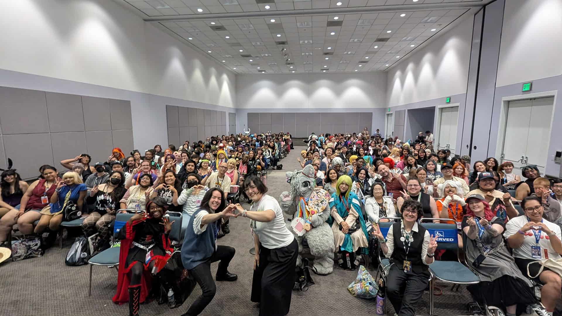 Manga Plaza Anime Expo | The Outerhaven Large group of cosplayers and attendees posing in a conference hall with gray walls and ceiling lights in the background.