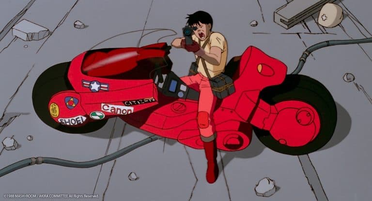 Person in a beige shirt and red pants sits on a bright red futuristic motorcycle, filming with a camera while riding.