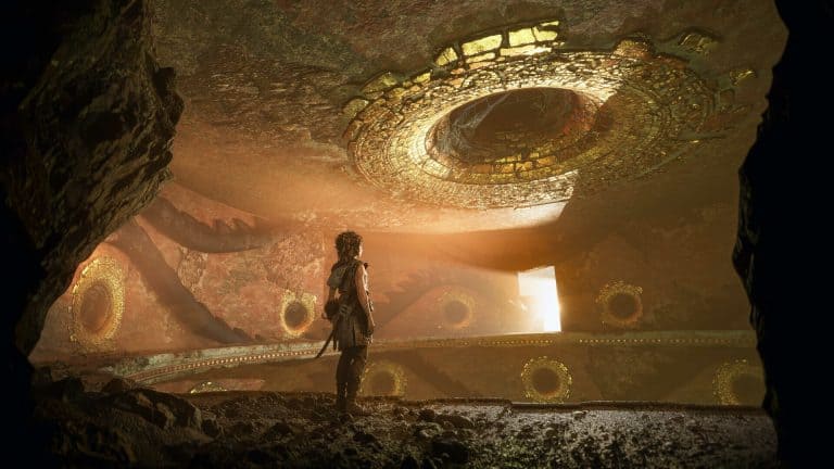 A Plague Tale Legacy | The Outerhaven A robed adventurer stands in a dim cavern with giant glowing circular stone rings on the walls above and around, illuminated by a warm light.