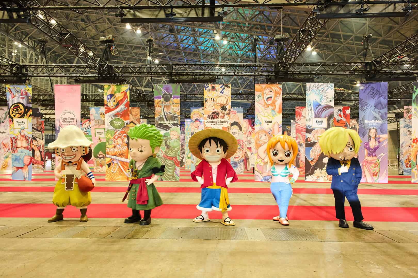 ONE PIECE | The Outerhaven Five colorful anime-style mascot costumes stand on a red carpet at a convention, with tall illustrated banners in the background.