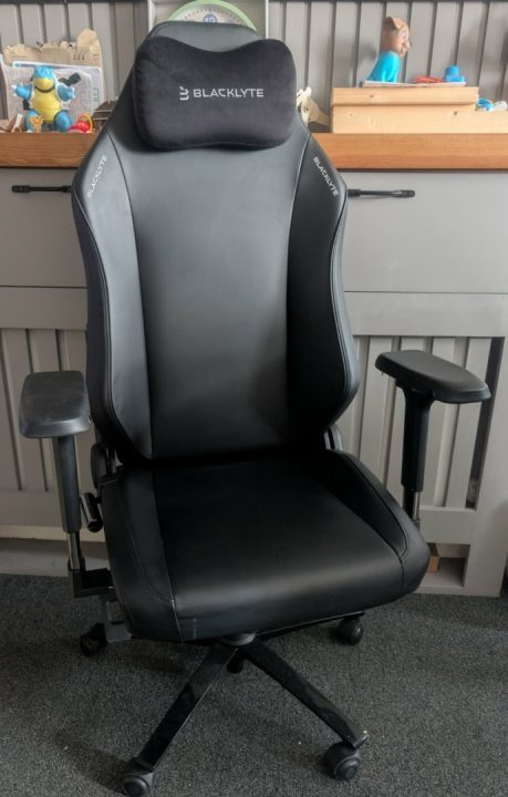 BAP Chair | The Outerhaven Black ergonomic gaming chair with padded headrest, adjustable arms, and a wheeled base in a home office setting