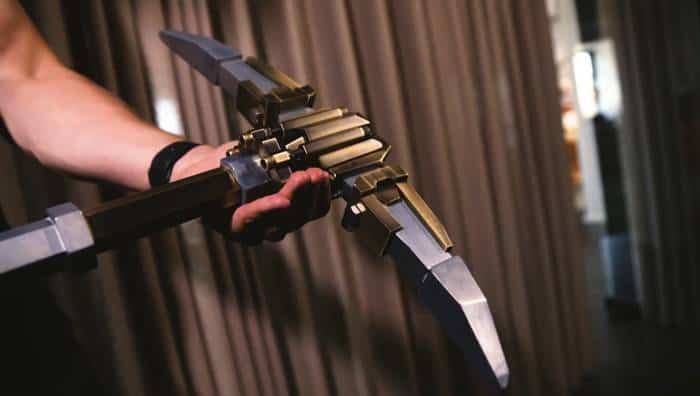 Deep Rock Galactic Metal Pickaxe Replica + New Merch Company Standard Pickaxe | The Outerhaven Close-up of a person gripping a large, futuristic metal blade-like prop with segmented segments and gears.”,
