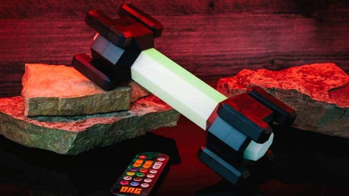 Deep Rock Galactic Metal Pickaxe Replica + New Merch Flare Lamp LEGO robotic arm built from white, black, and red bricks rests on stacked rocks with a remote nearby under red lighting.