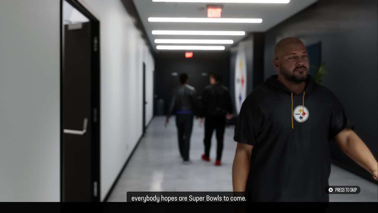EA SPORTS™ Madden NFL 27-Coach Cutscene A muscular man in a Pittsburgh Steelers hoodie stands in a dim hallway, with blurred figures in the background.