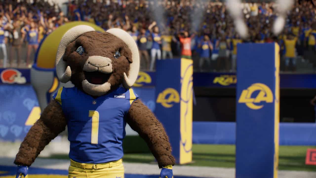 EA SPORTS™ Madden NFL 27-Ram Masc Rams mascot in blue and yellow uniform on the football field with cheering fans in the stands behind him.