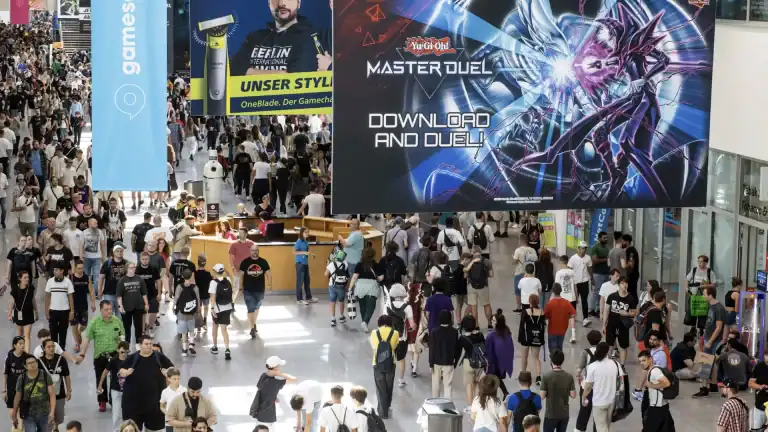 Gamescom 2026 - Showroom Floor Image | The Outerhaven Crowded convention hall with tall banners and a large Yu-Gi-Oh Master Duel poster overhead (people walking and browsing stalls).