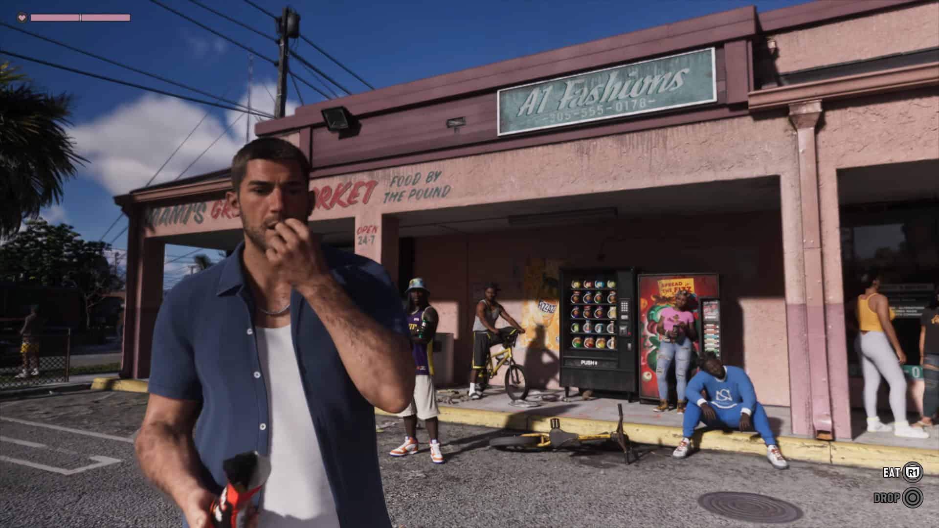 Grand Theft Auto VI - Jason is snacking | The Outerhaven Man in a blue shirt eats a snack outside a pink storefront with a sign ‘A1 Fashions’, vending machine and bystanders in the background.